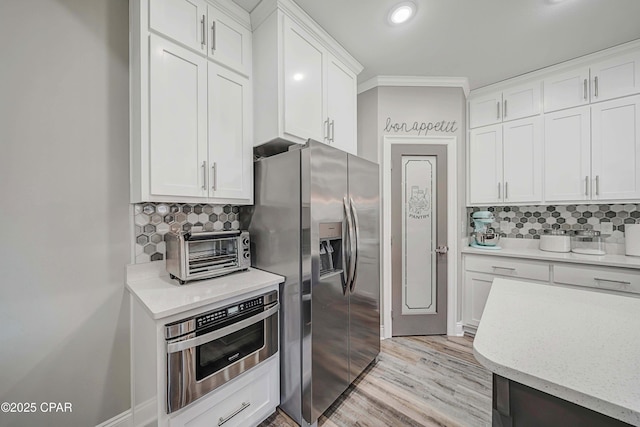 kitchen with appliances with stainless steel finishes, white cabinetry, tasteful backsplash, ornamental molding, and light wood-type flooring