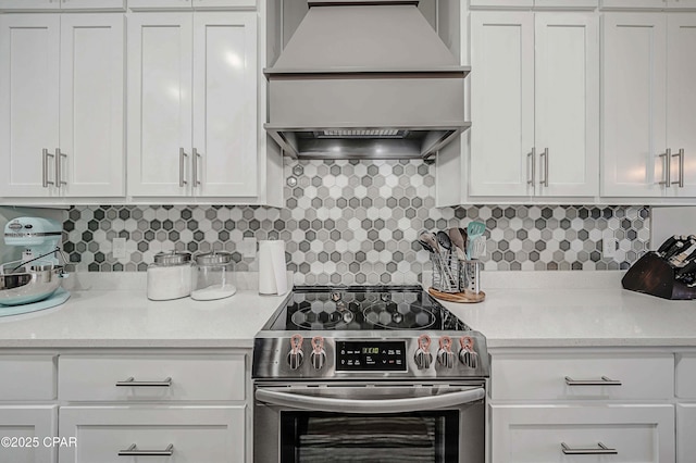 kitchen featuring tasteful backsplash, electric range, white cabinetry, and custom range hood