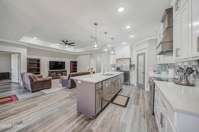 kitchen with ceiling fan, sink, hanging light fixtures, appliances with stainless steel finishes, and an island with sink