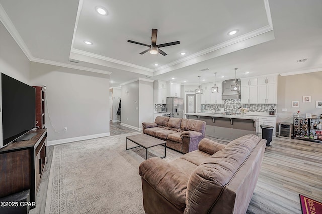 living room featuring ceiling fan, crown molding, light hardwood / wood-style flooring, and a raised ceiling