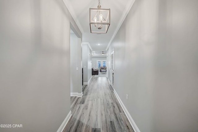 corridor featuring light wood-type flooring, crown molding, and an inviting chandelier