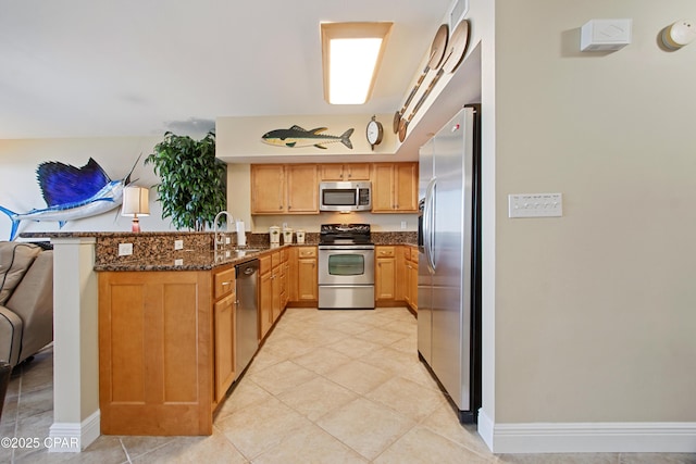kitchen featuring kitchen peninsula, dark stone counters, stainless steel appliances, sink, and light tile patterned floors