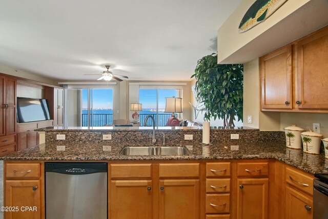 kitchen with stainless steel dishwasher, ceiling fan, dark stone countertops, and sink