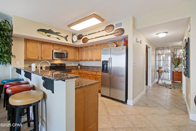 kitchen featuring kitchen peninsula, a kitchen breakfast bar, stainless steel appliances, and dark stone counters