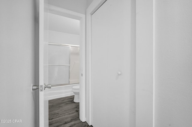 bathroom with hardwood / wood-style flooring, toilet, and enclosed tub / shower combo