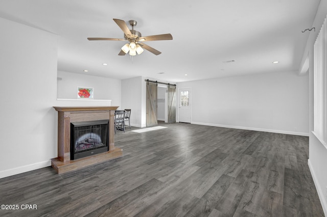 unfurnished living room with a barn door, ceiling fan, and dark wood-type flooring