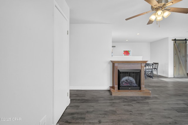 unfurnished living room featuring ceiling fan, a barn door, and dark hardwood / wood-style flooring