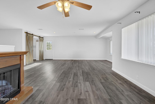 unfurnished living room featuring a barn door, ceiling fan, and dark hardwood / wood-style floors