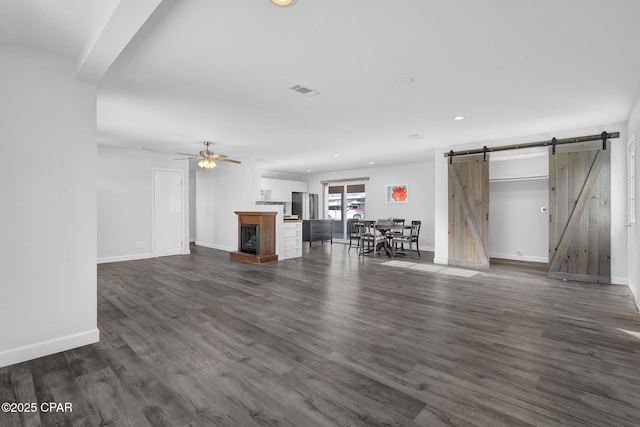 unfurnished living room featuring dark hardwood / wood-style floors, a barn door, a multi sided fireplace, and ceiling fan