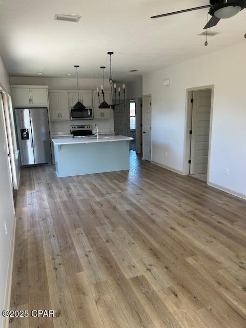 kitchen with hanging light fixtures, ceiling fan, light hardwood / wood-style floors, stainless steel appliances, and a center island with sink