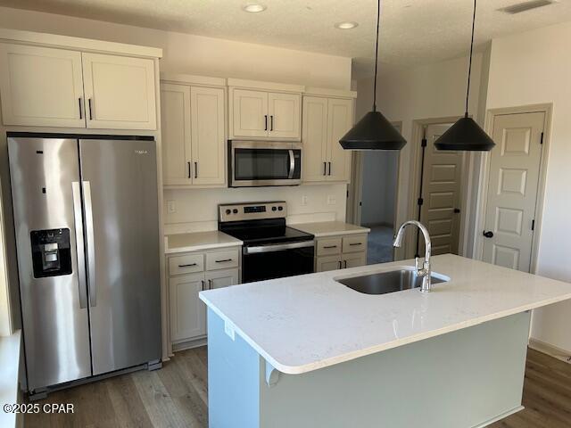 kitchen featuring white cabinets, sink, an island with sink, appliances with stainless steel finishes, and decorative light fixtures