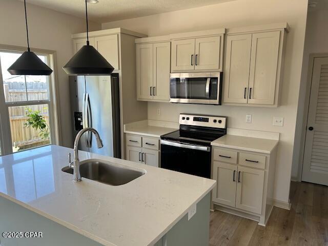 kitchen with decorative light fixtures, sink, hardwood / wood-style flooring, a kitchen island with sink, and stainless steel appliances