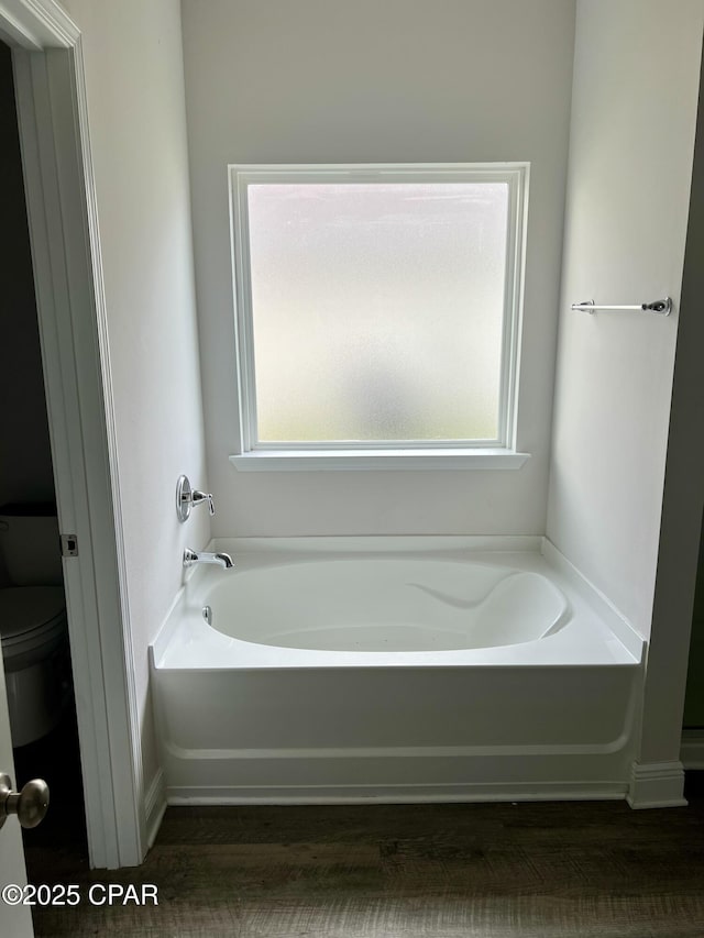 bathroom with hardwood / wood-style flooring, plenty of natural light, toilet, and a bathtub