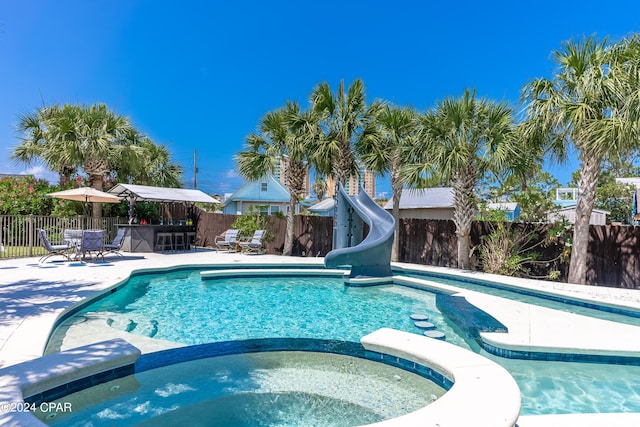 view of pool with an in ground hot tub, a water slide, an outdoor bar, and a patio area