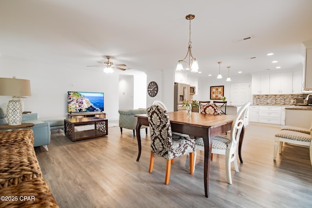 dining room featuring light wood-type flooring and ceiling fan with notable chandelier