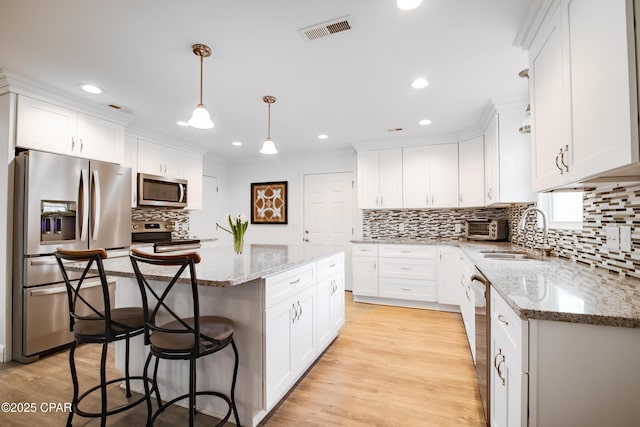 kitchen featuring pendant lighting, a kitchen island, white cabinetry, and appliances with stainless steel finishes