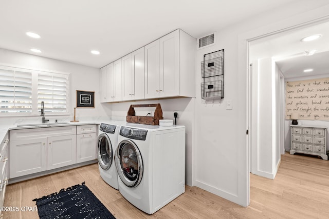 laundry room featuring washer and clothes dryer, cabinets, light wood-type flooring, and sink