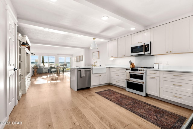 kitchen with kitchen peninsula, appliances with stainless steel finishes, sink, light hardwood / wood-style floors, and white cabinetry