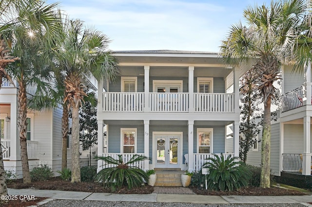 coastal home with a porch, a balcony, and french doors