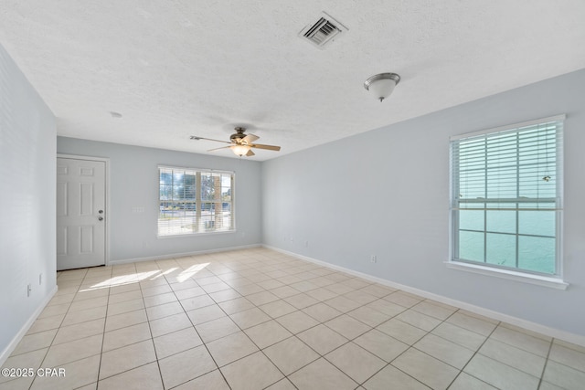 empty room with plenty of natural light, ceiling fan, light tile patterned flooring, and a textured ceiling