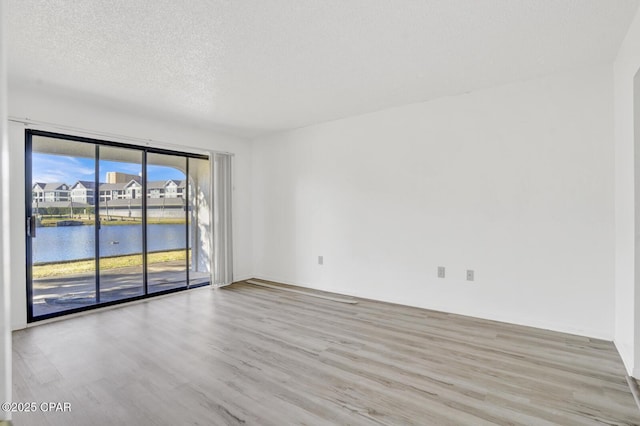 spare room featuring a textured ceiling, light hardwood / wood-style floors, and a water view