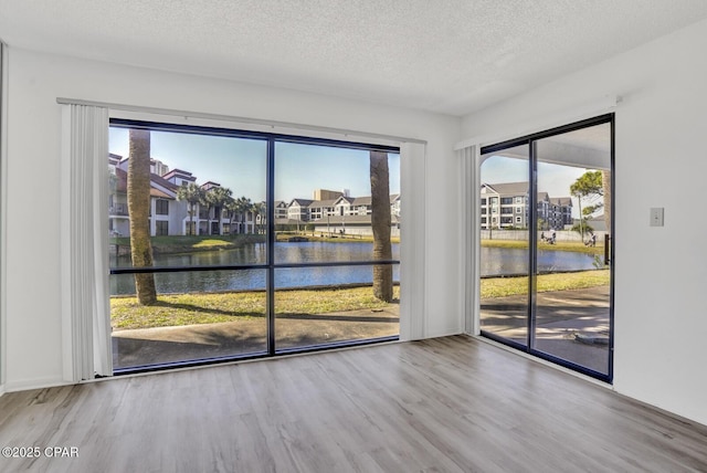 spare room with a wealth of natural light, a textured ceiling, wood-type flooring, and a water view