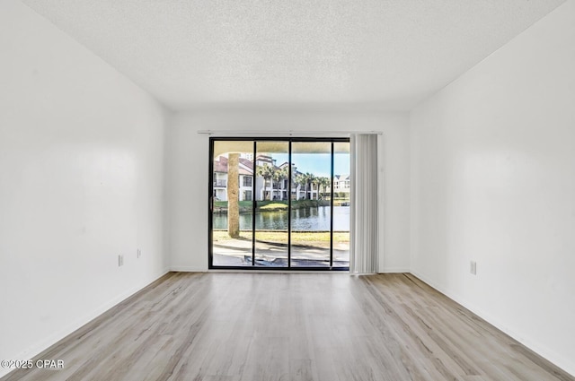 empty room featuring a textured ceiling, light wood-type flooring, and a water view