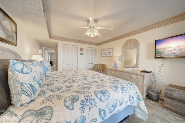 bedroom with a textured ceiling, light hardwood / wood-style flooring, multiple closets, ceiling fan, and ornamental molding