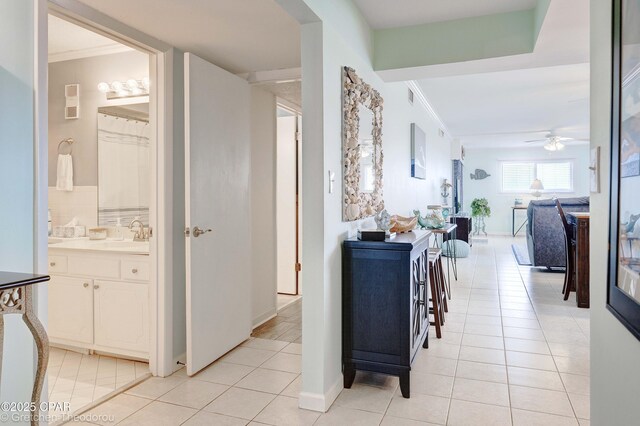 corridor featuring sink, light tile patterned floors, and crown molding