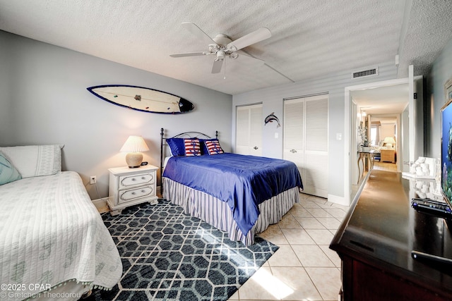 bedroom featuring a textured ceiling, ceiling fan, light tile patterned floors, and multiple closets