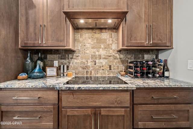 kitchen featuring tasteful backsplash, black electric stovetop, custom exhaust hood, and light stone countertops