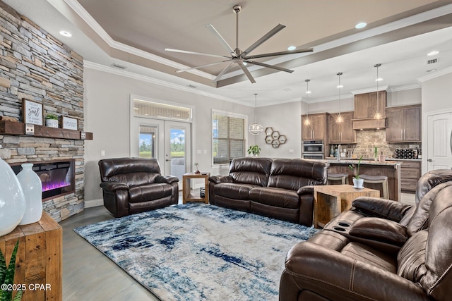 living room with a stone fireplace, ornamental molding, a raised ceiling, and ceiling fan