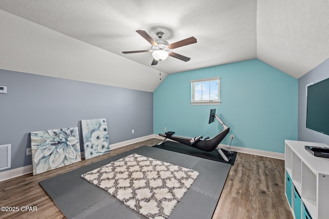 exercise area with ceiling fan, dark hardwood / wood-style flooring, vaulted ceiling, and a textured ceiling