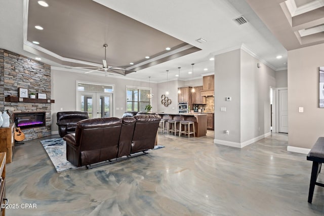 living room with crown molding, ceiling fan, concrete flooring, a stone fireplace, and a raised ceiling