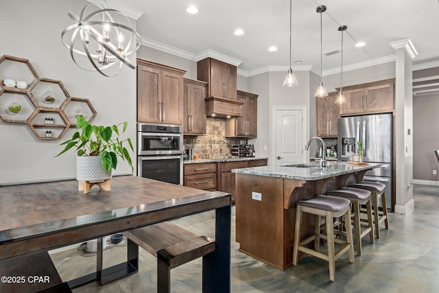 kitchen with light stone counters, pendant lighting, stainless steel appliances, a kitchen island with sink, and backsplash