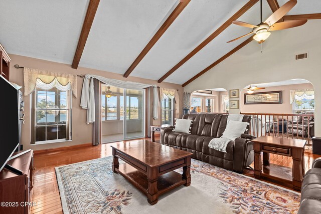 living room featuring beamed ceiling, light wood-type flooring, high vaulted ceiling, and ceiling fan