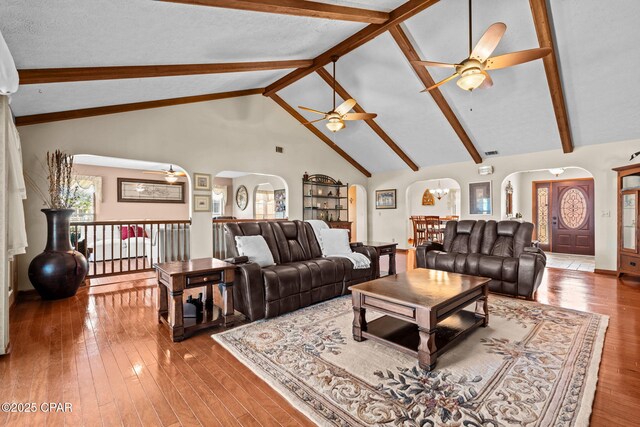 living room featuring ceiling fan with notable chandelier, wood-type flooring, beam ceiling, and high vaulted ceiling