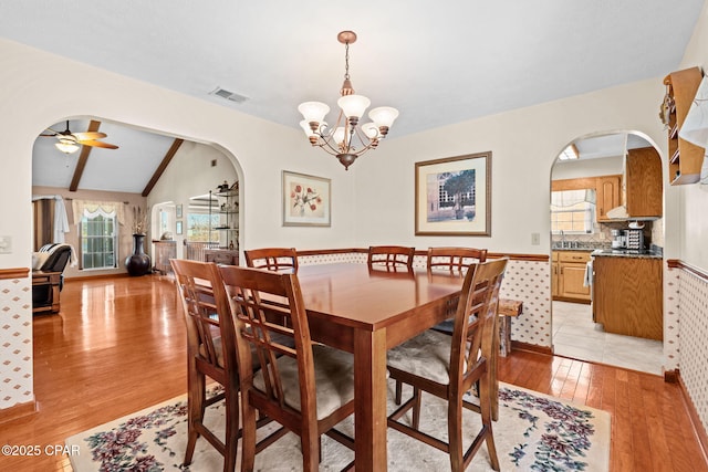 dining area featuring lofted ceiling with beams, sink, light wood-type flooring, and ceiling fan with notable chandelier