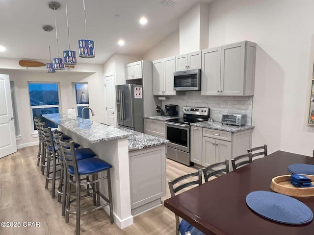 145 Turtle Walk Unit 60, Port St Joe, FL 32456 - kitchen with appliances with stainless steel finishes, a center island with sink, decorative backsplash, a kitchen bar, and light wood-type flooring