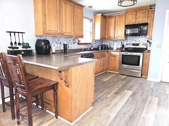 kitchen featuring kitchen peninsula, decorative light fixtures, a kitchen bar, stainless steel range with electric cooktop, and light wood-type flooring