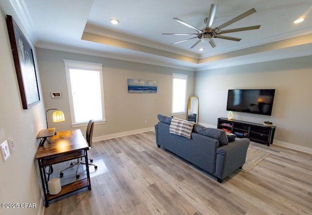 living room featuring light wood-type flooring, ornamental molding, and a tray ceiling