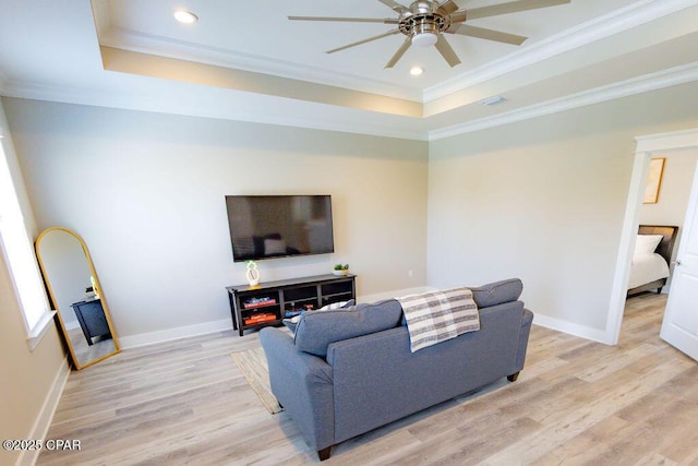 living room featuring light wood-type flooring, a tray ceiling, ceiling fan, and ornamental molding