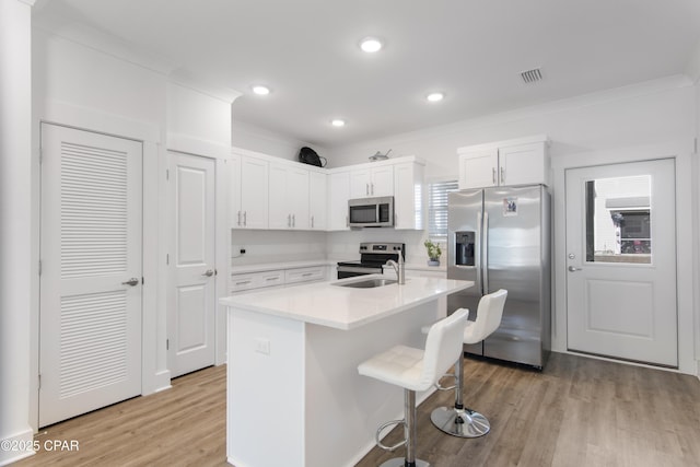 kitchen with white cabinetry, light wood-type flooring, a kitchen island with sink, stainless steel appliances, and a kitchen breakfast bar