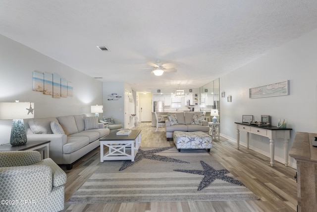 living room with a ceiling fan, wood finished floors, visible vents, and baseboards