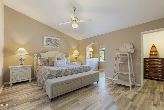 bedroom with lofted ceiling, light wood-style flooring, arched walkways, and baseboards