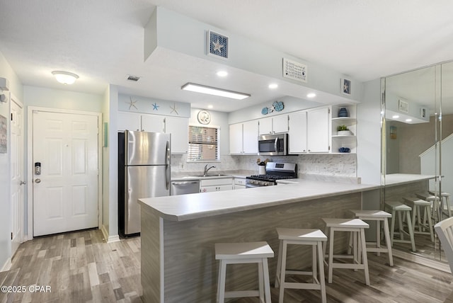 kitchen featuring tasteful backsplash, kitchen peninsula, sink, white cabinetry, and appliances with stainless steel finishes