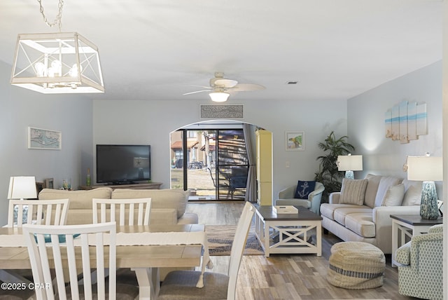 living room with ceiling fan with notable chandelier, wood finished floors, visible vents, and arched walkways