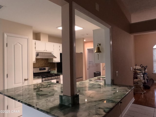 kitchen featuring stainless steel range with gas cooktop, white cabinets, refrigerator, dark stone countertops, and backsplash