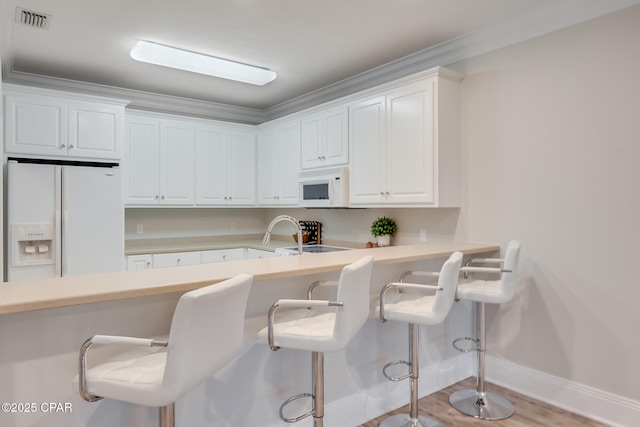 kitchen featuring white cabinetry, a kitchen bar, and white appliances