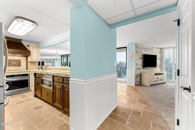 kitchen with a drop ceiling, custom range hood, light carpet, kitchen peninsula, and appliances with stainless steel finishes